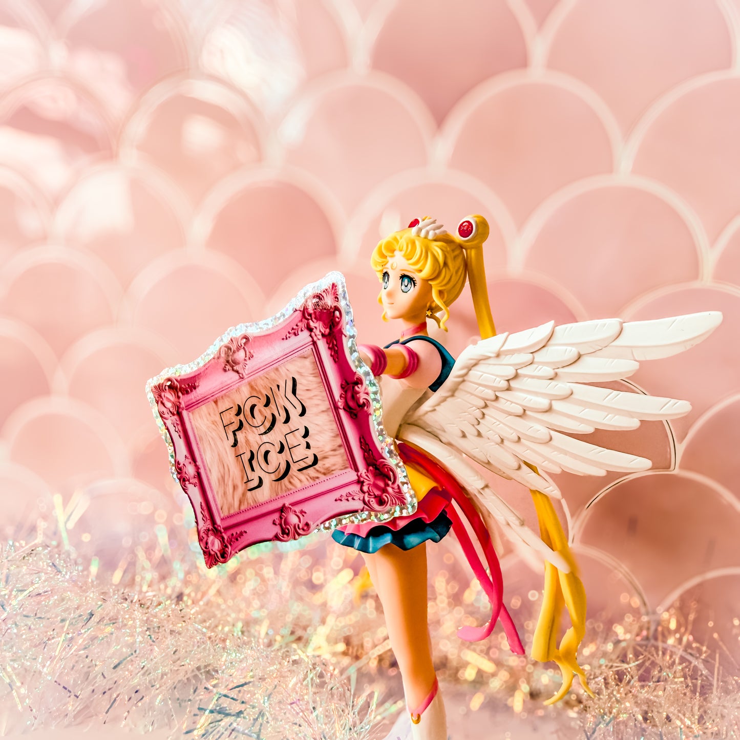 Toy figure with wings holding a pink mirror displaying 'FCK ICE' against a pink background