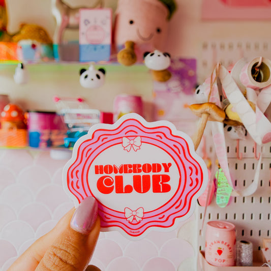 Hand holding a 'Nobody Club' sticker in front of a colorful background with stationery items.