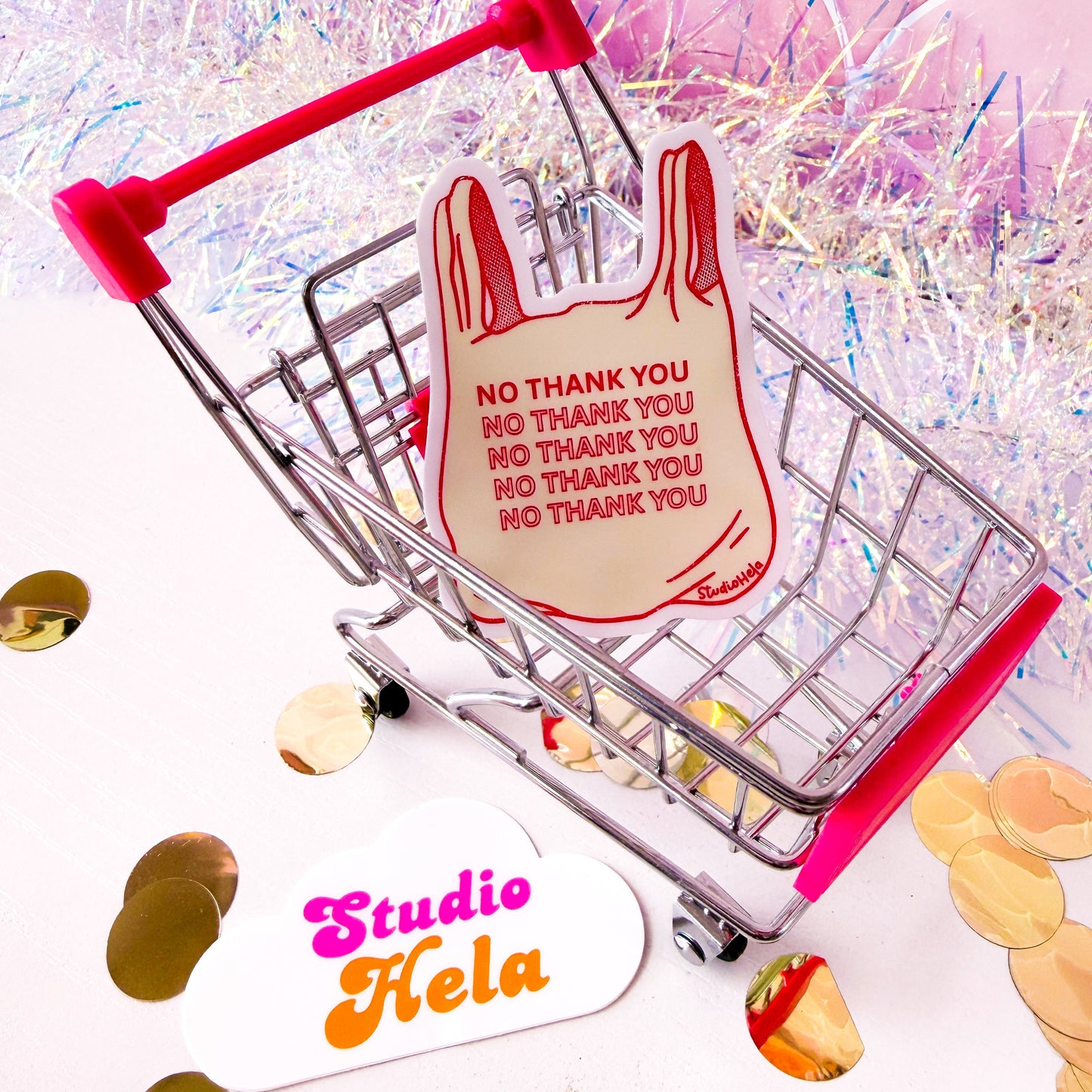 Small shopping cart with a red bag labeled 'No Thank You' from Studio Hela on a colorful background.