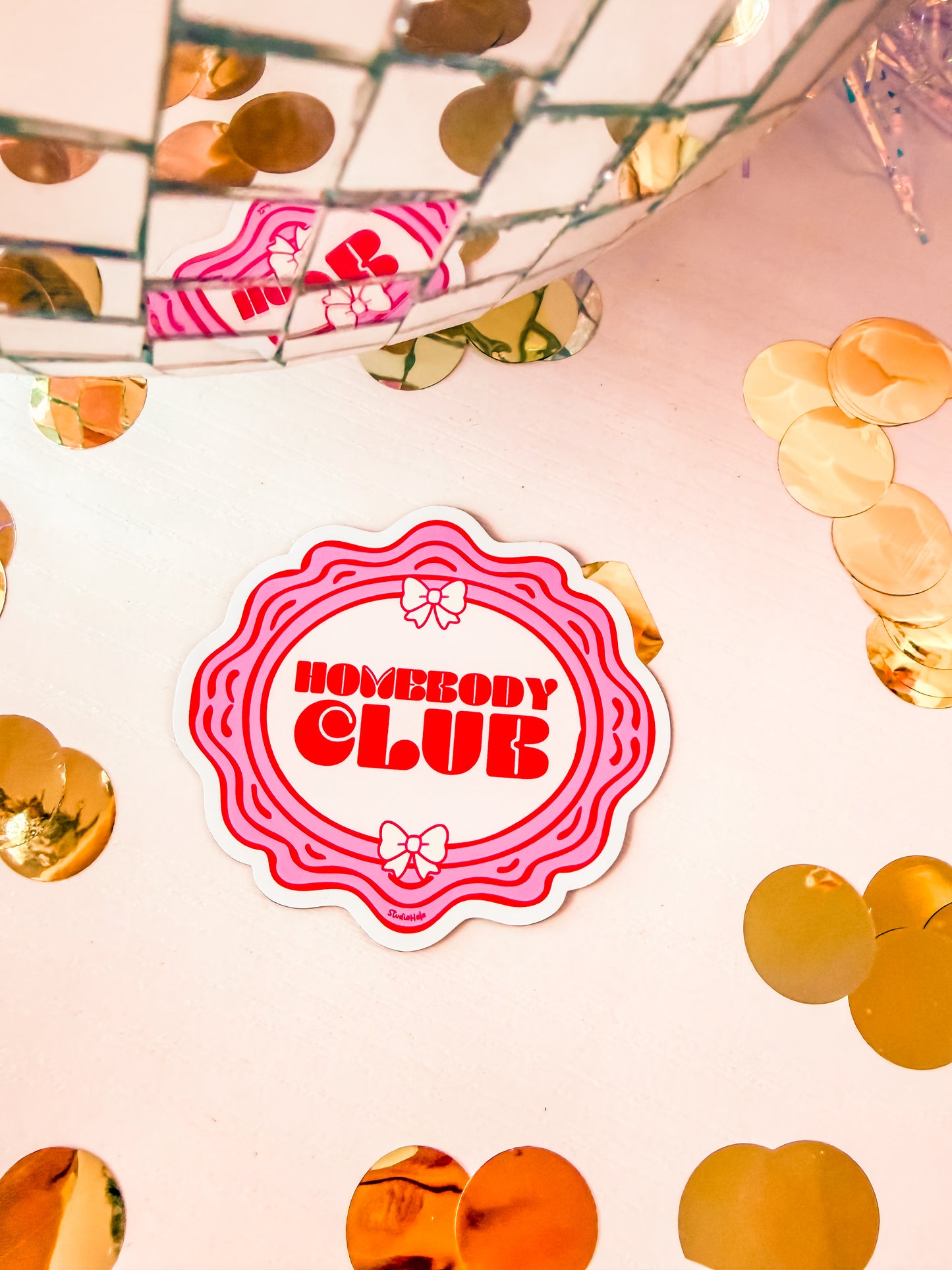 Sticker with 'Homebody Club' text on a pink background with decorative elements.