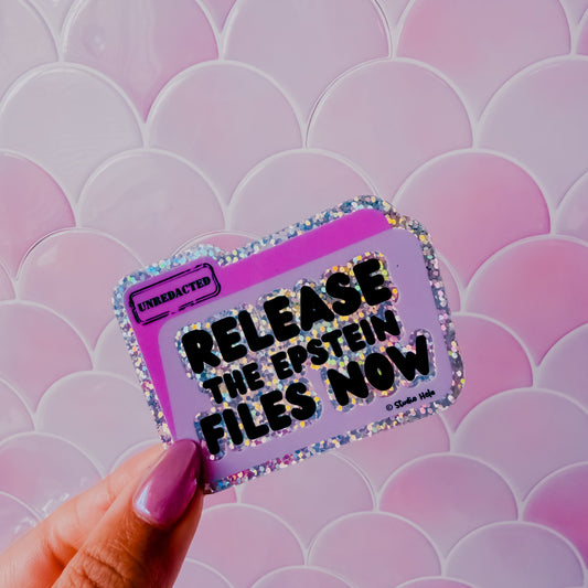 Hand holding a colorful sticker with text against a pink and white patterned background