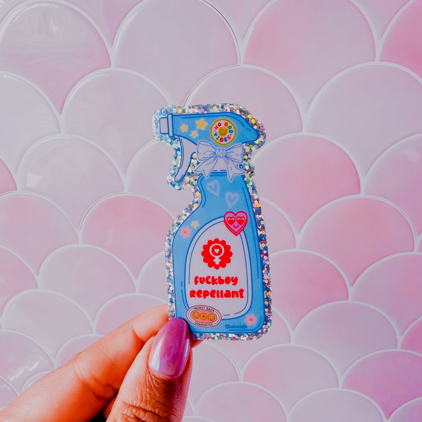 Spray bottle-shaped keychain labeled 'fuckboy Repellent' held against a pink and white patterned background.
