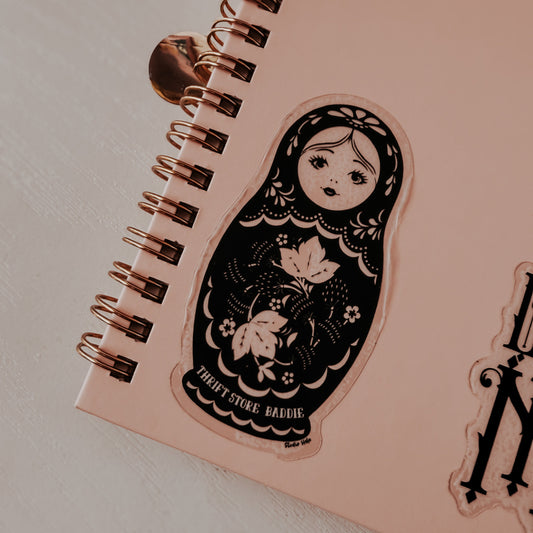 Pink notebook with a decorative sticker of a matryoshka doll on a light background