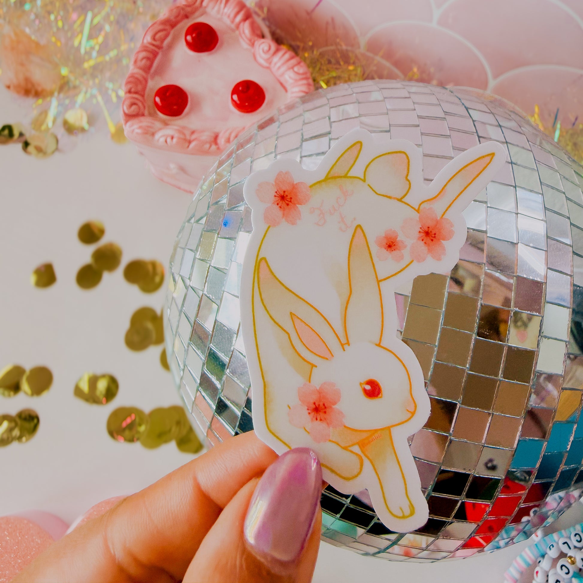 Hand holding a disco ball with a rabbit sticker on a colorful background