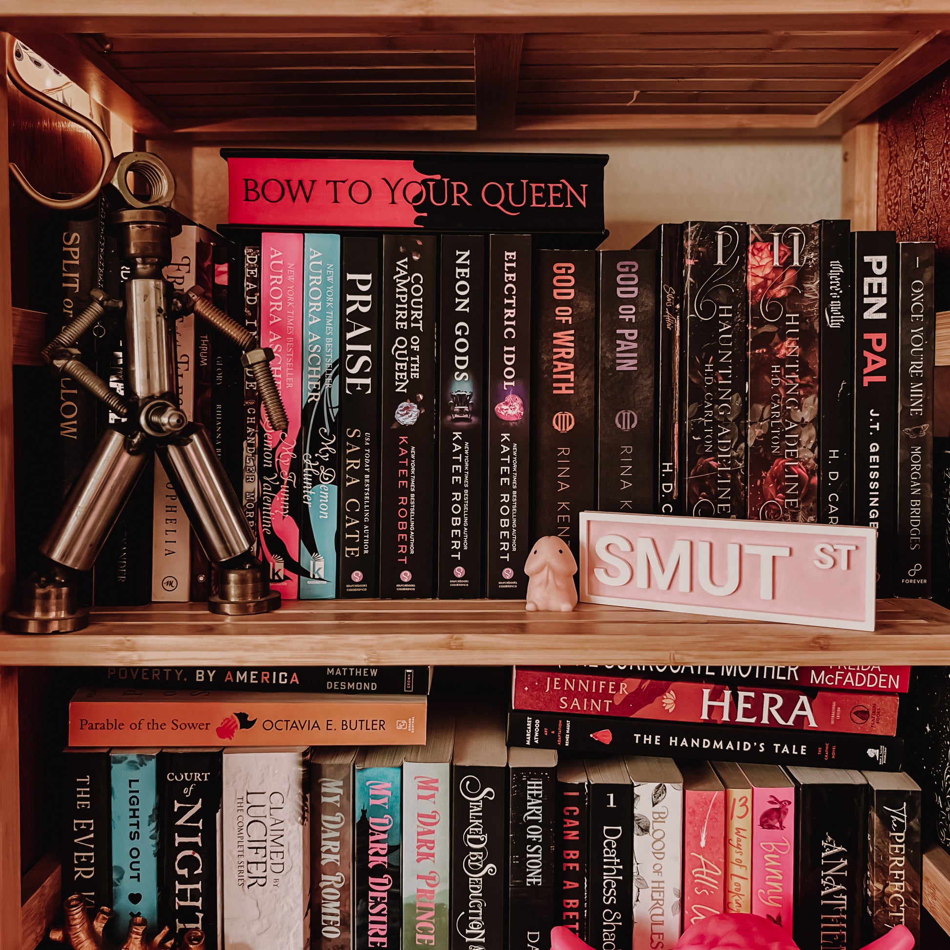 Bookshelf with a variety of books and decorative items, including a small sculpture and a 'Smut St' sign.