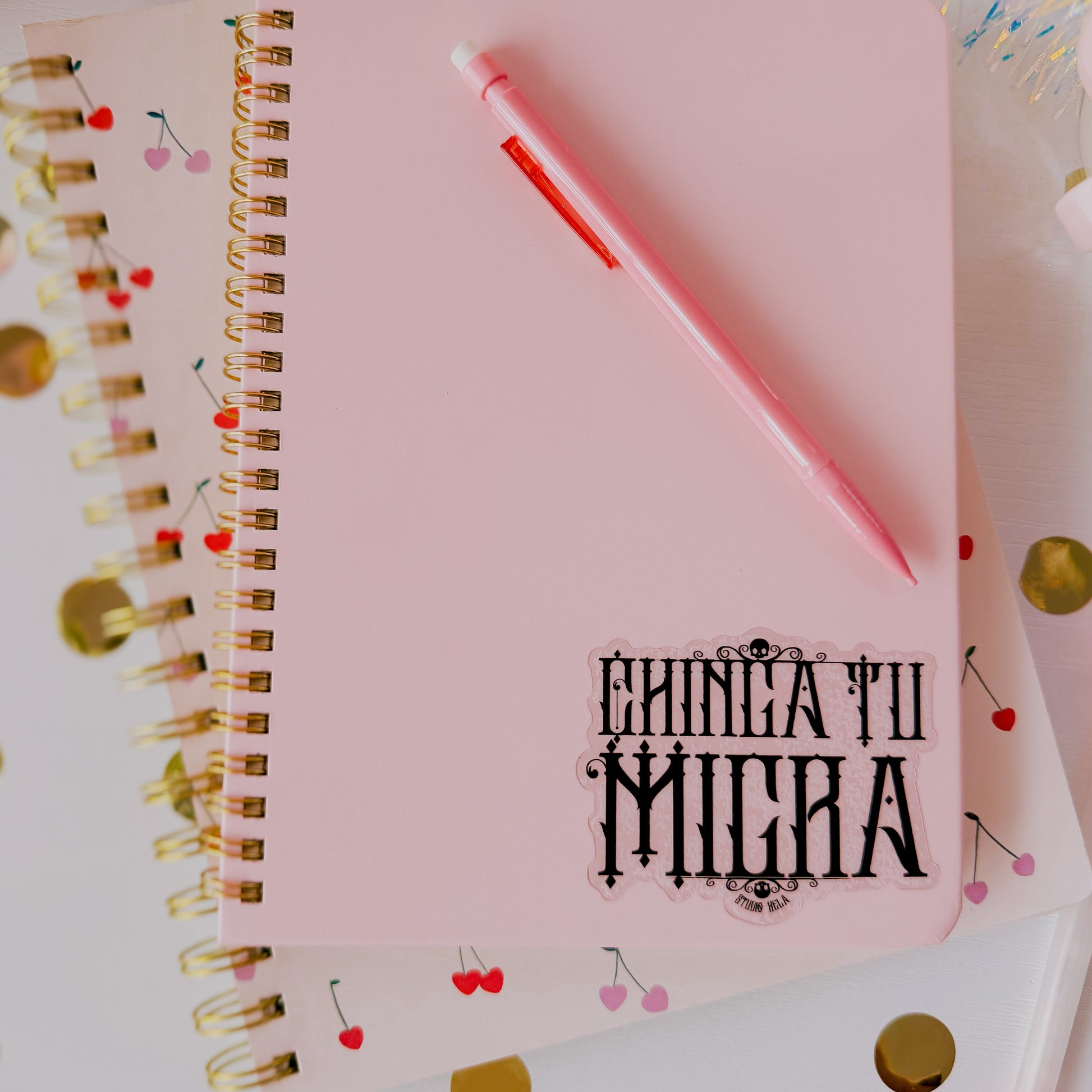Pink notebook with 'Chica Tu Mija' text and a pink pen on a colorful confetti background