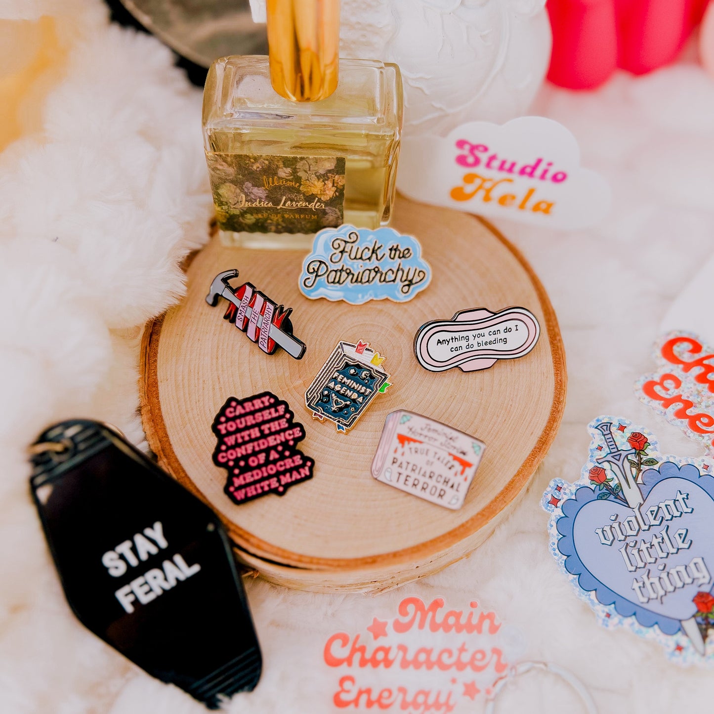 This image features a collection of enamel pins displayed on a wooden round tray, which adds an artistic touch to the presentation. The pins vary in design and message, ranging from a bold "SMASH THE PATRIARCHY" to others that are more decorative in nature.