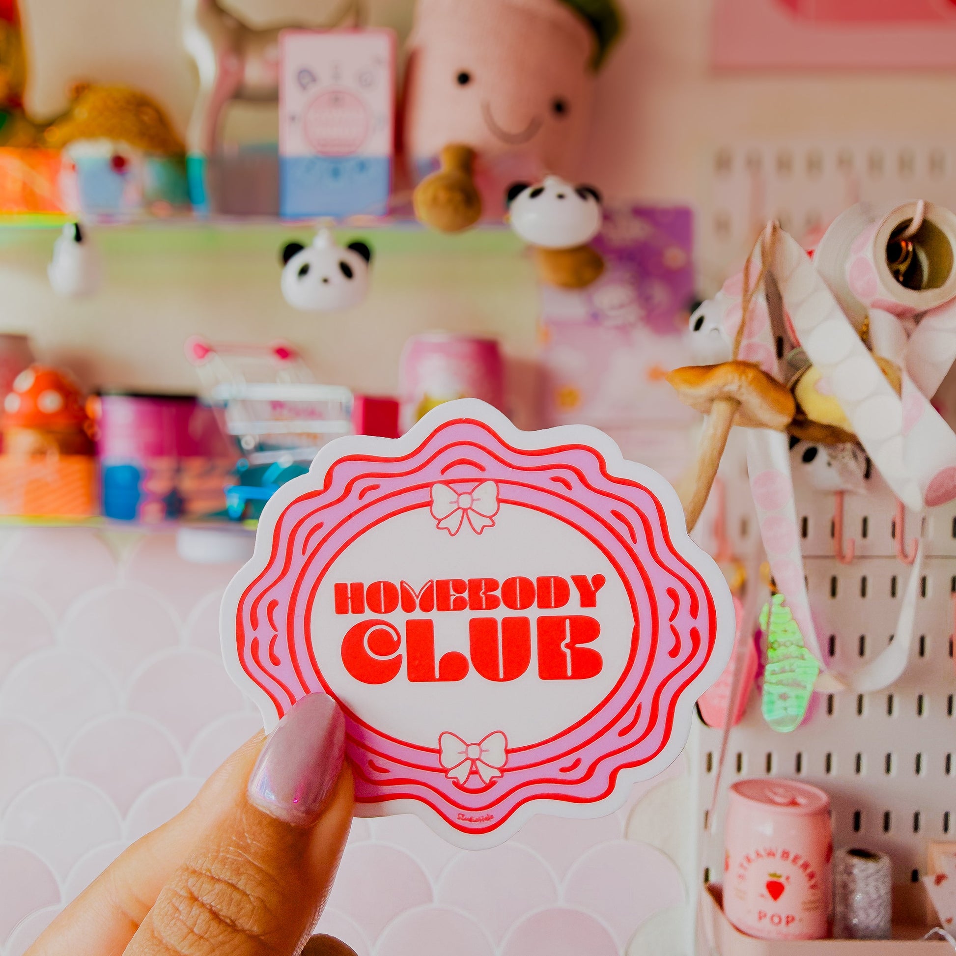 Hand holding a 'Nobody Club' sticker in front of a colorful background with stationery items.