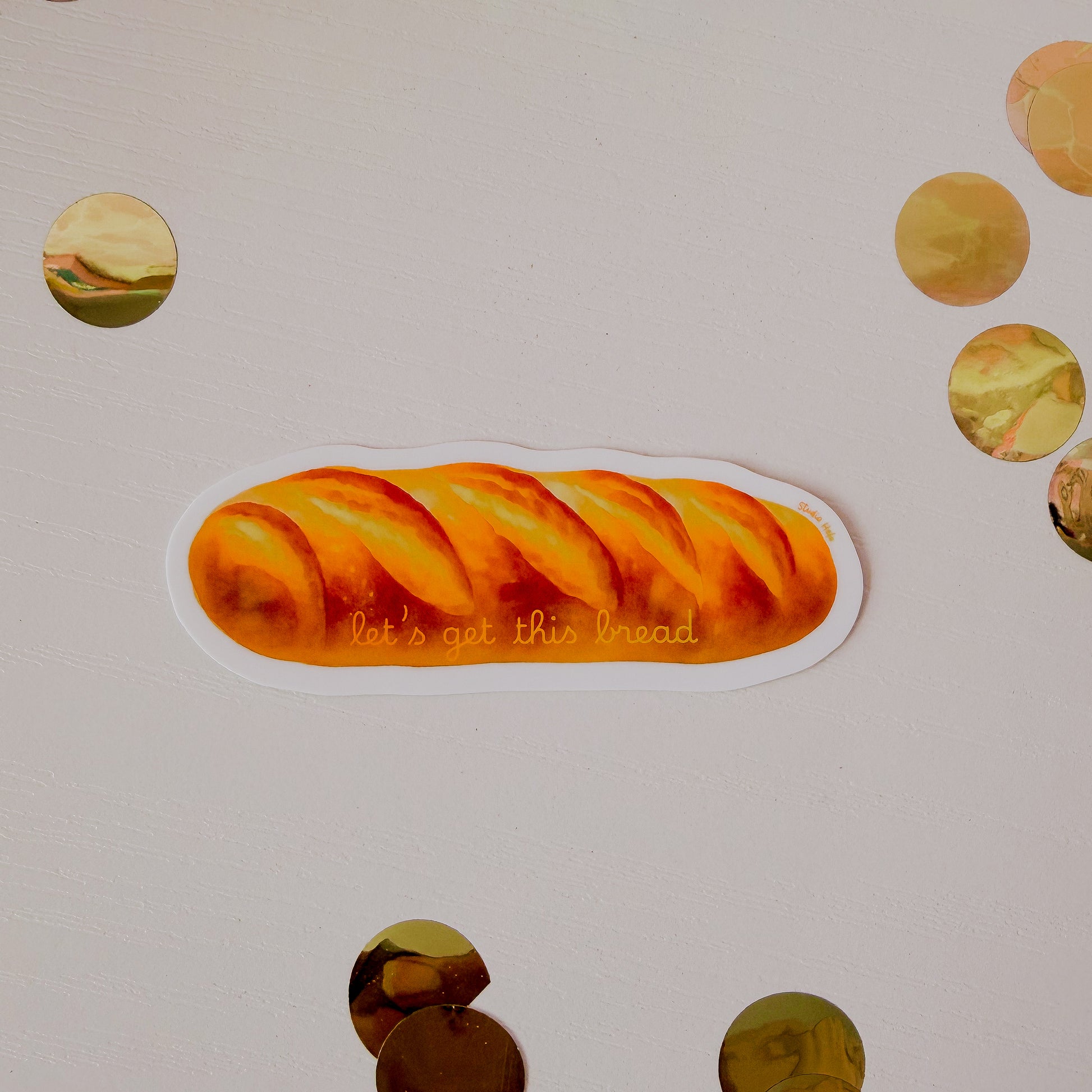 Sticker of a loaf of bread with the text 'let's eat this bread' on a beige background.