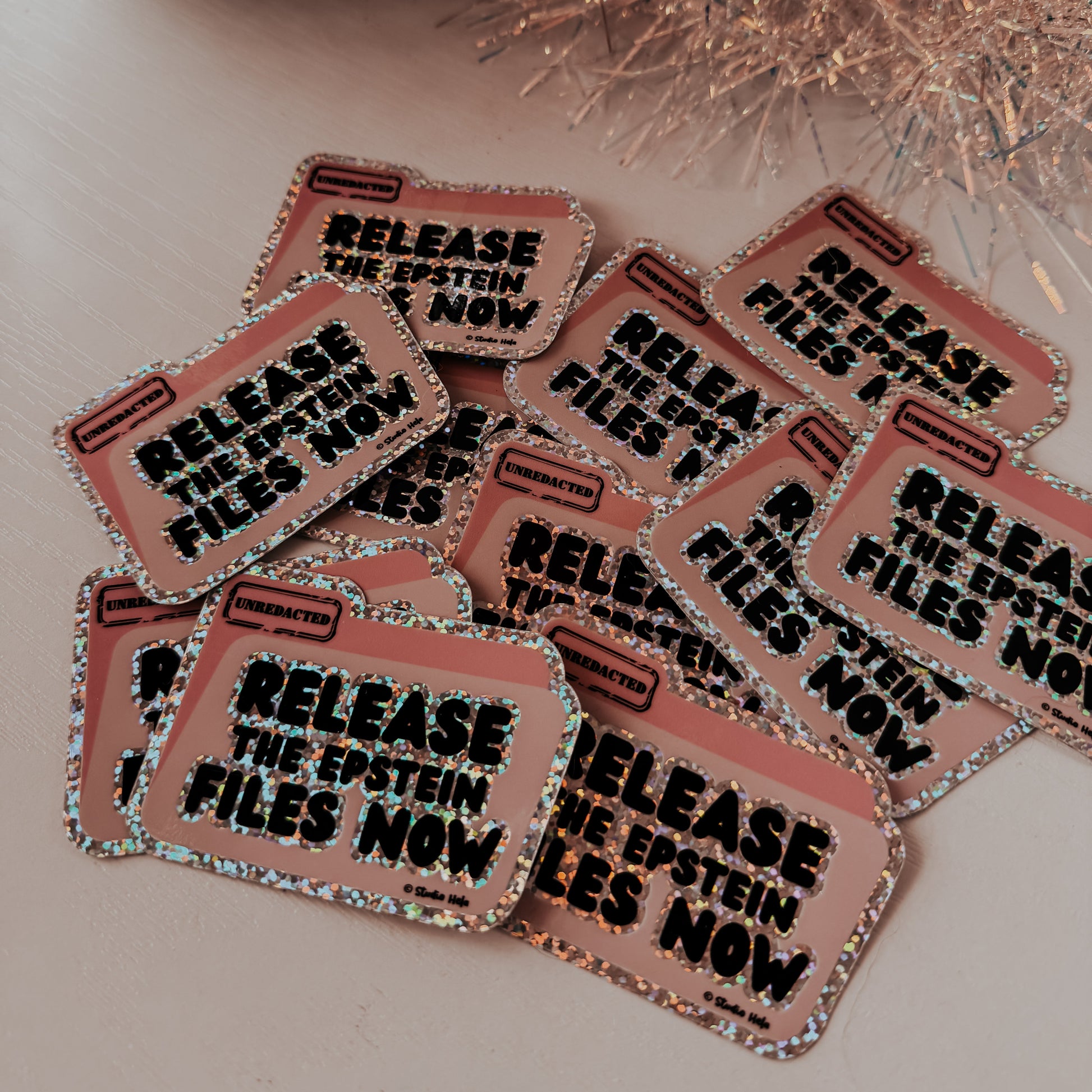 Stickers with 'Release the Epstein files now' text on a reflective surface with decorative elements.