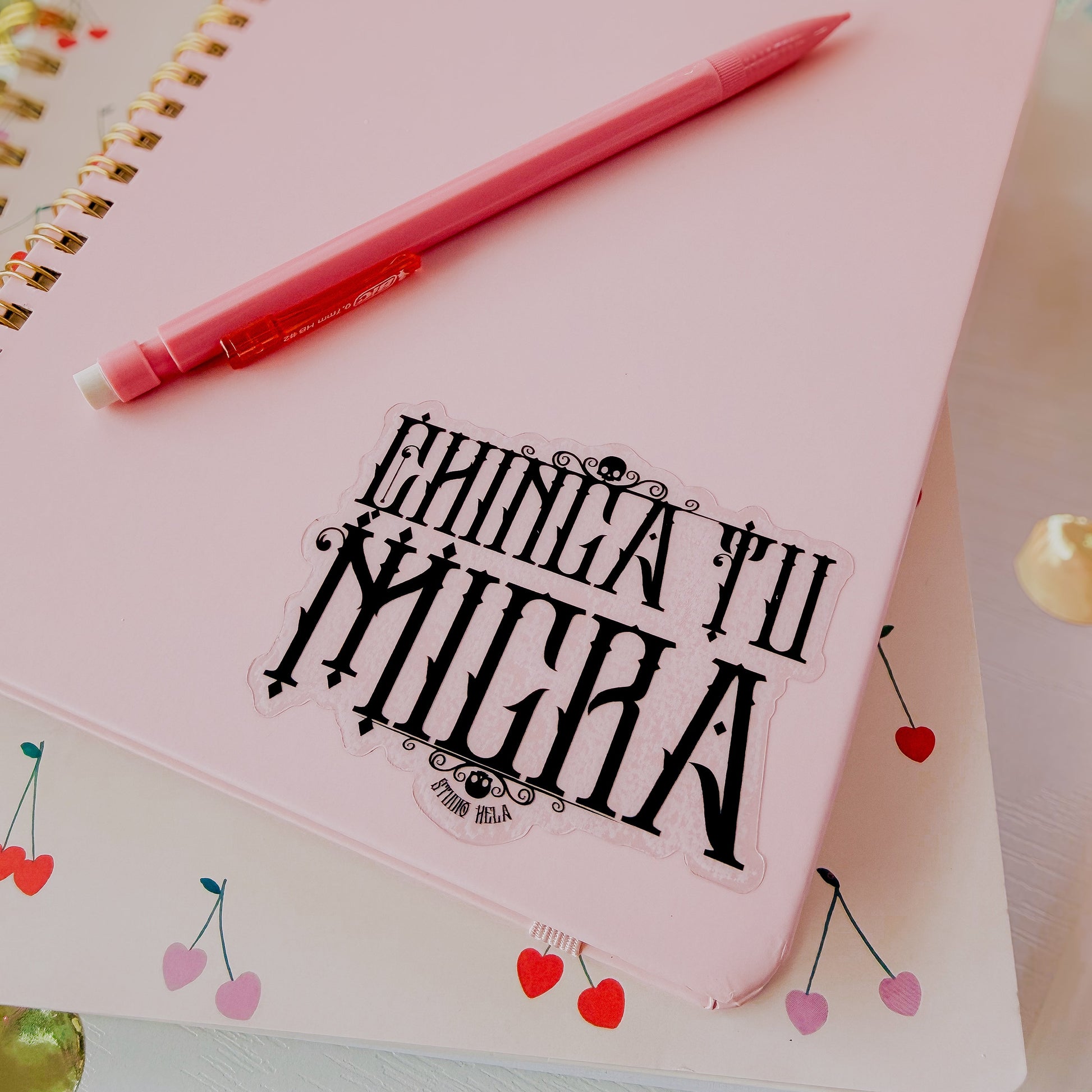 Pink notebook with a red pen on top, featuring decorative elements and text.