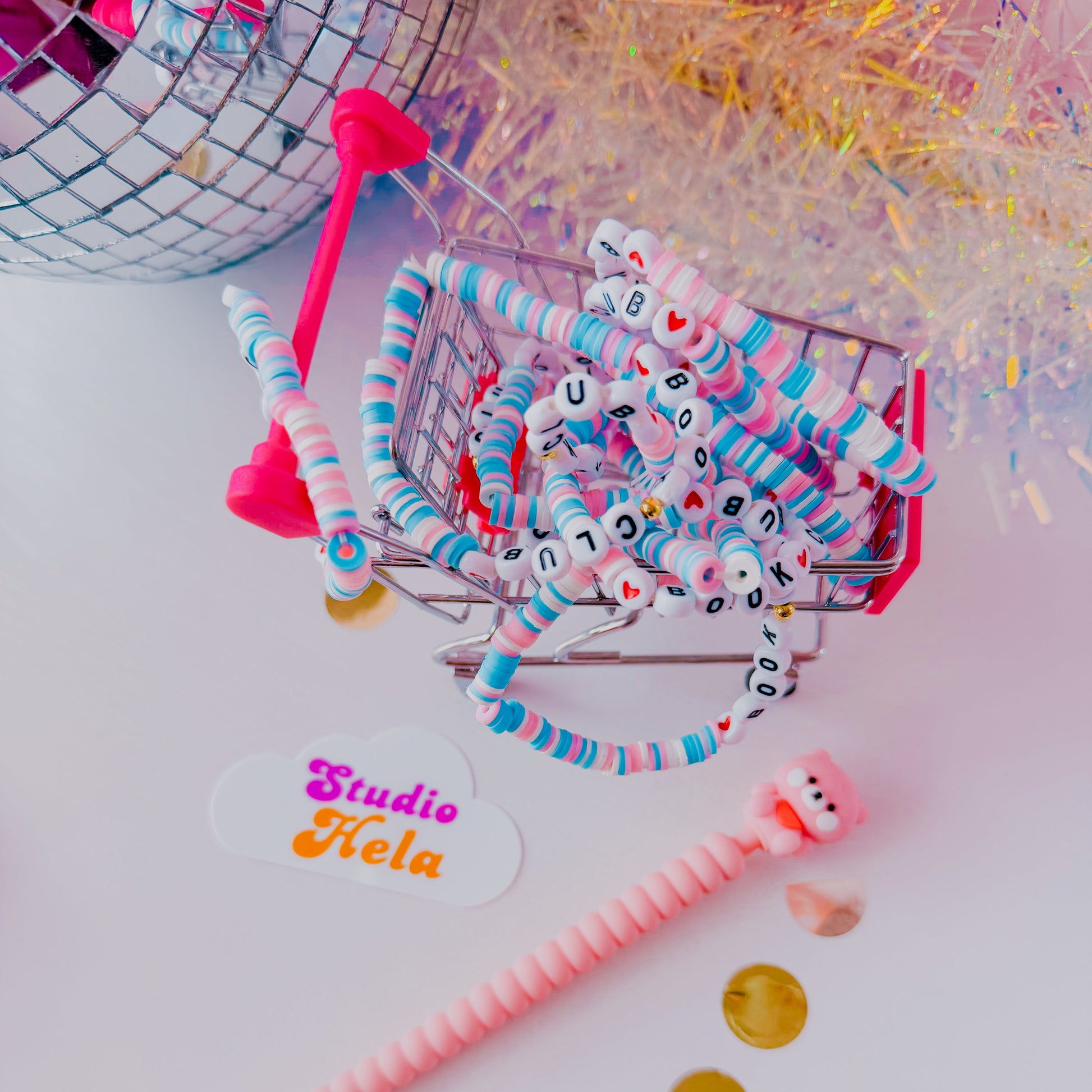 Colorful party accessories including a disco ball, straws, and a small shopping cart on a white background with 'Studio Hela' branding.