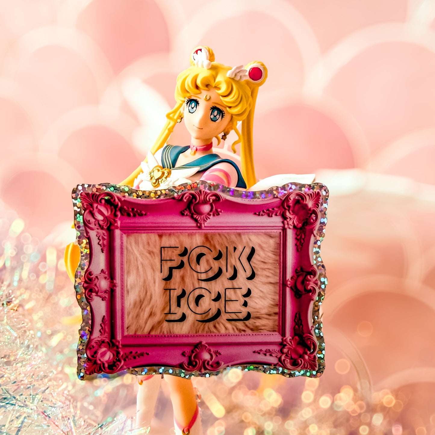 Figurine holding a pink frame with 'FCK ICE' text against a blurred background