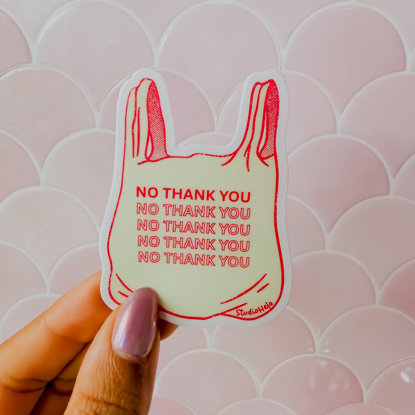 Hand holding a sticker with 'No Thank You' text against a pink patterned background