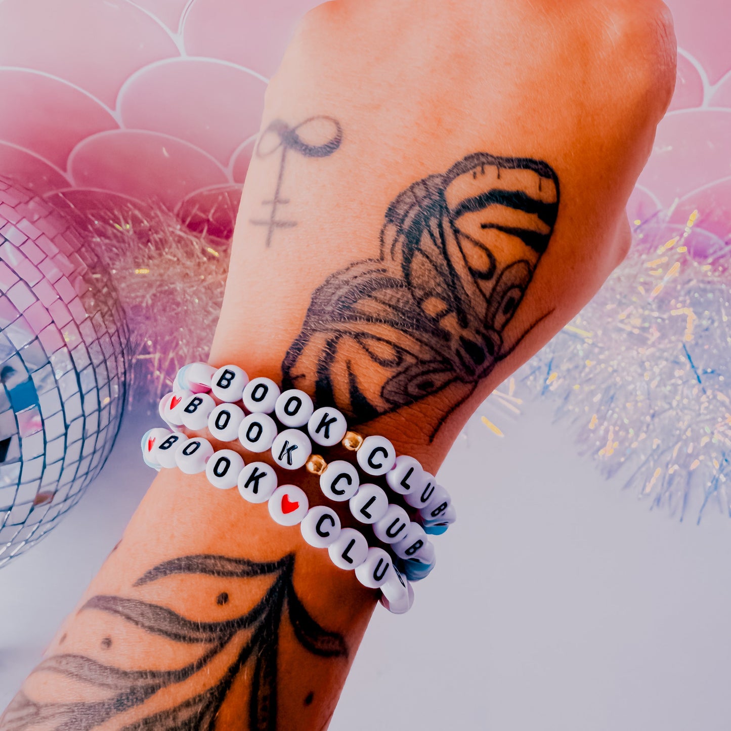 Hand with butterfly tattoo wearing multiple bracelets on a colorful background