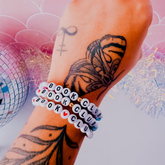 Hand with butterfly tattoo wearing multiple bracelets on a colorful background