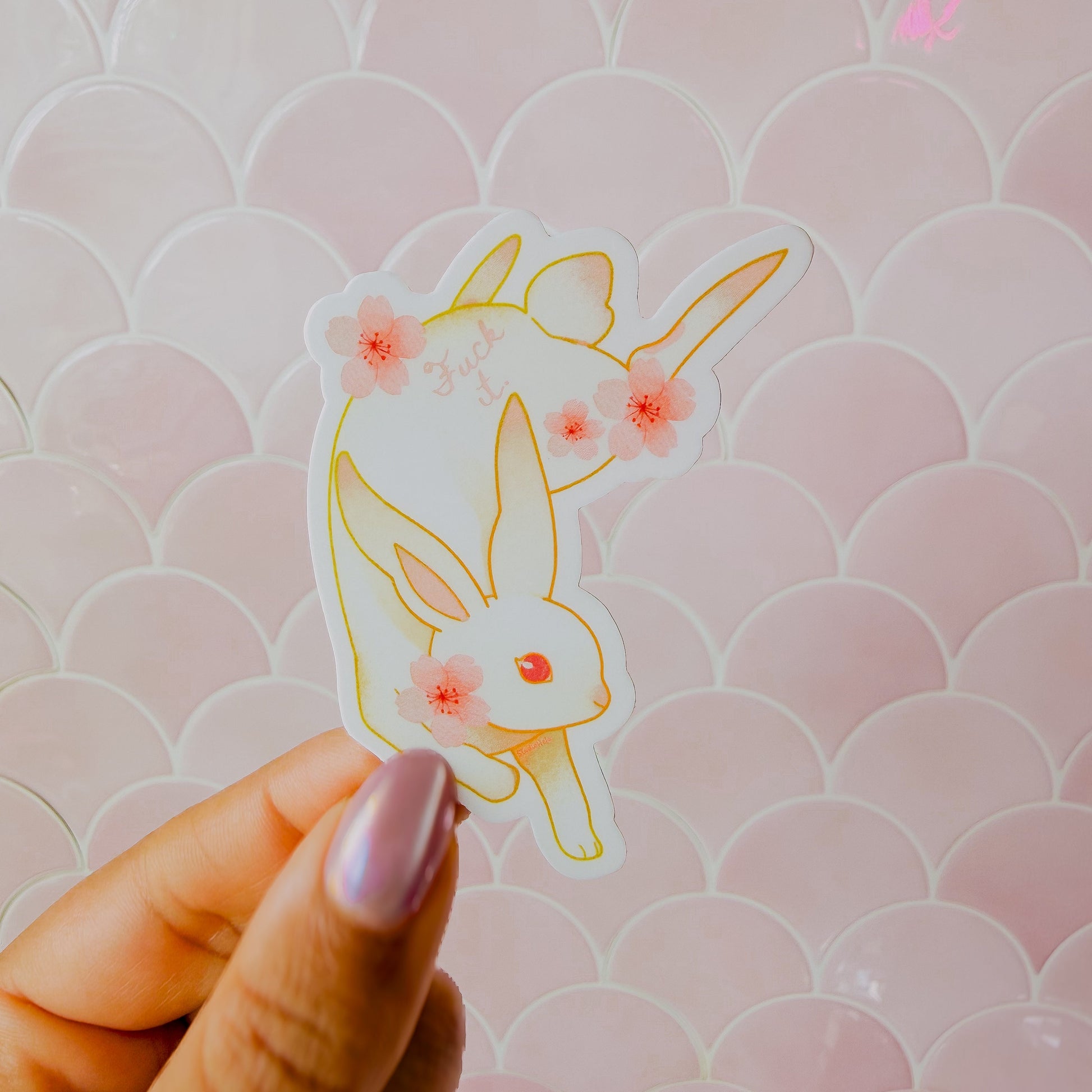 Hand holding a rabbit-shaped sticker with floral details against a pink patterned background