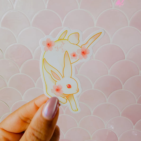 Hand holding a rabbit-shaped sticker with floral details against a pink patterned background