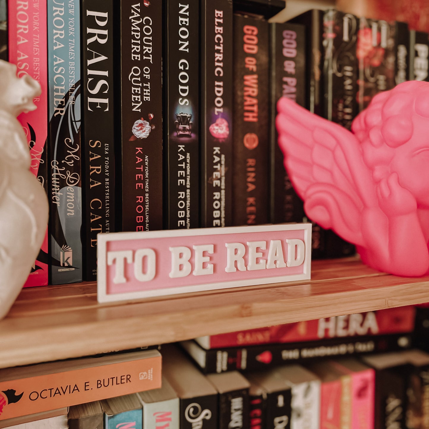 Bookshelf with books and a pink 'To Be Read' sign
