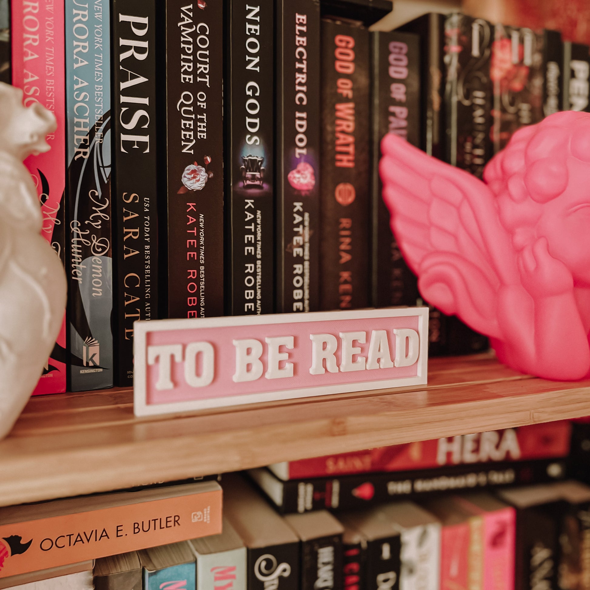 Bookshelf with books and a pink 'To Be Read' sign
