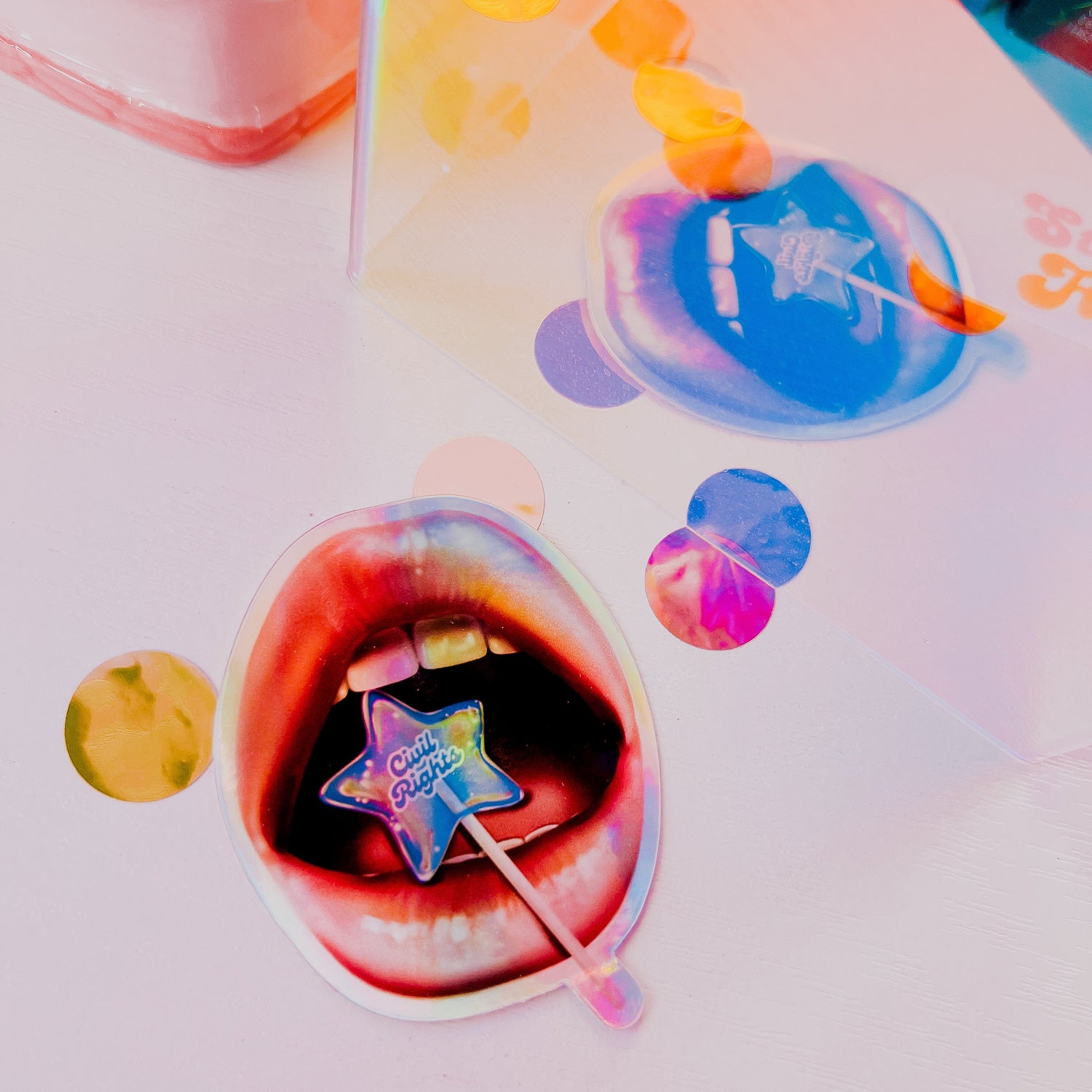 This image features a striking 3-inch vinyl holographic sticker with the theme of civil rights. The sticker showcases an artistic depiction of a mouth with vibrant, multicolored lips, holding a popsicle that blends seamlessly into the colorful background.