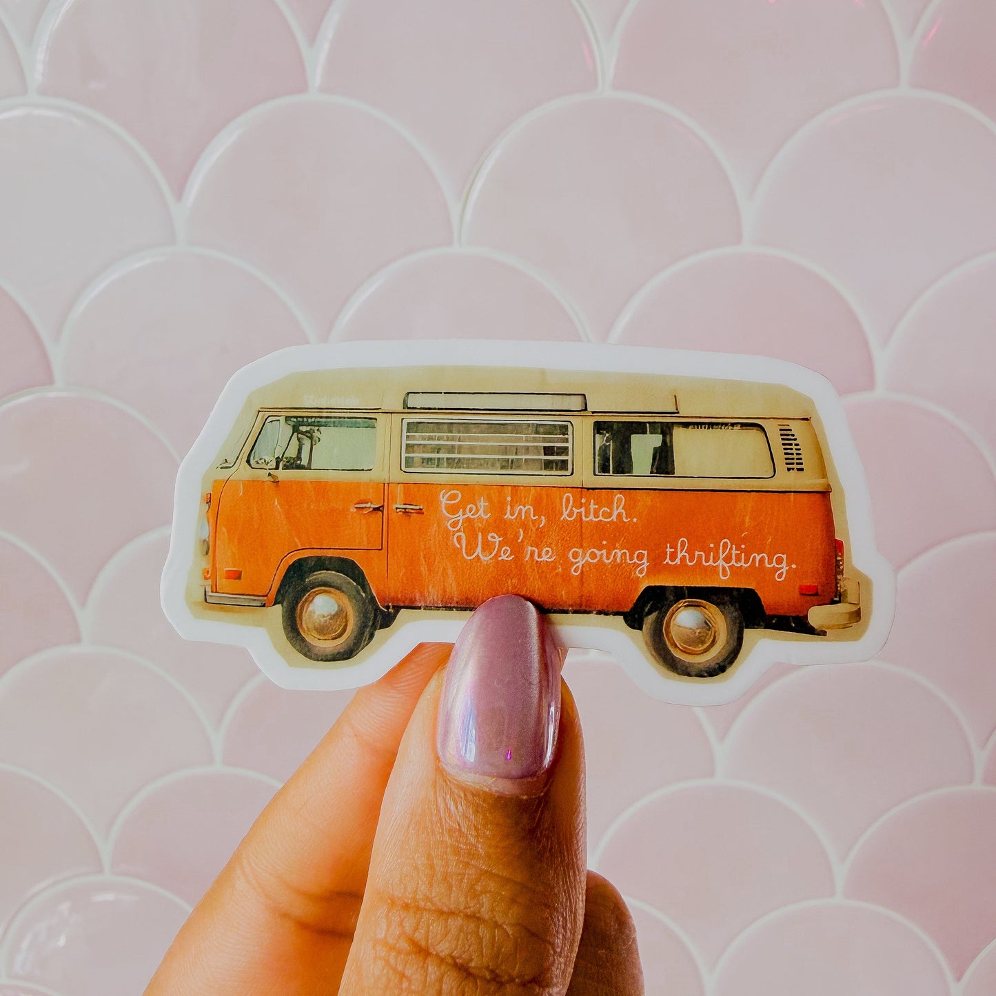 Hand holding a sticker of an orange van with text against a pink patterned background