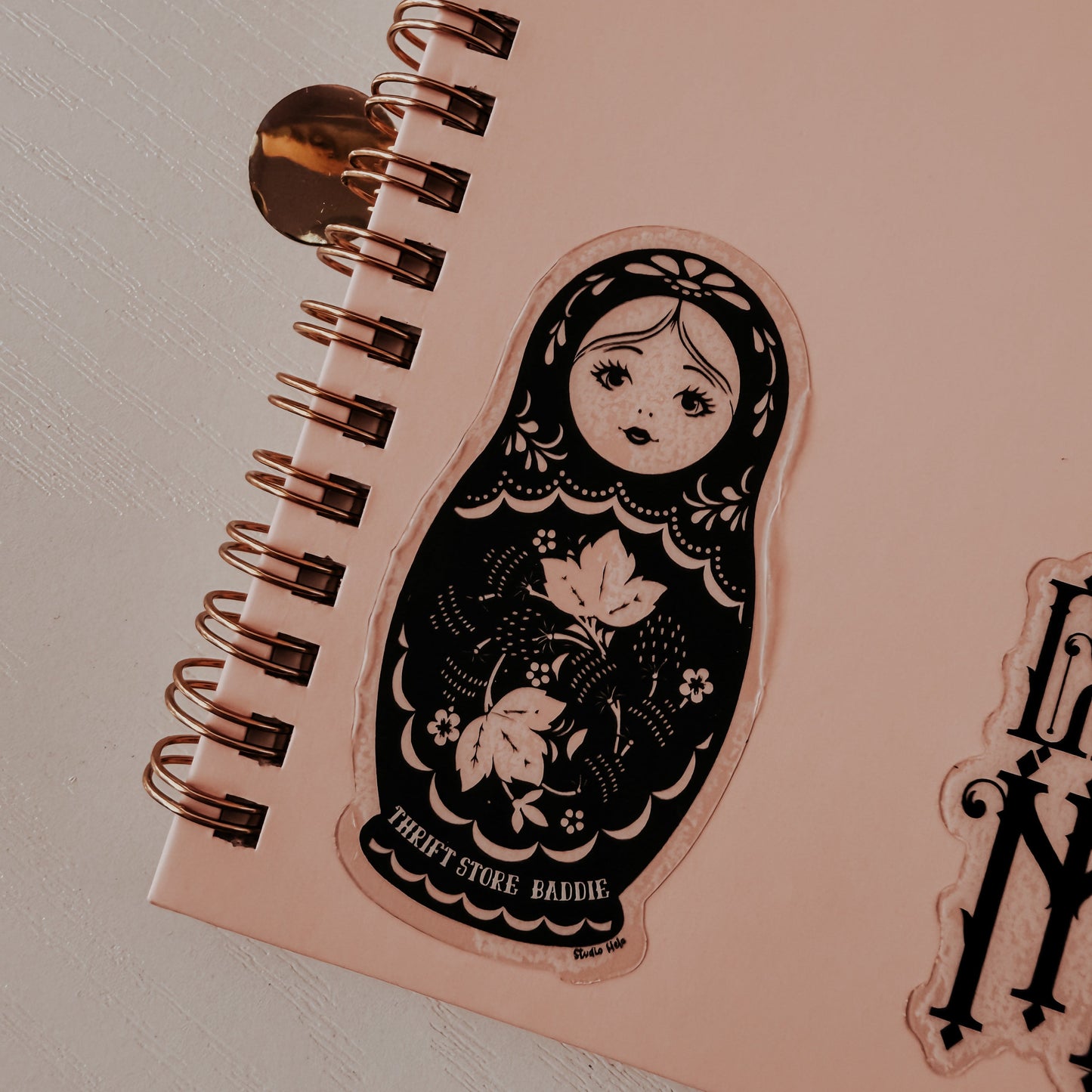 Pink notebook with a decorative sticker of a matryoshka doll on a light gray background