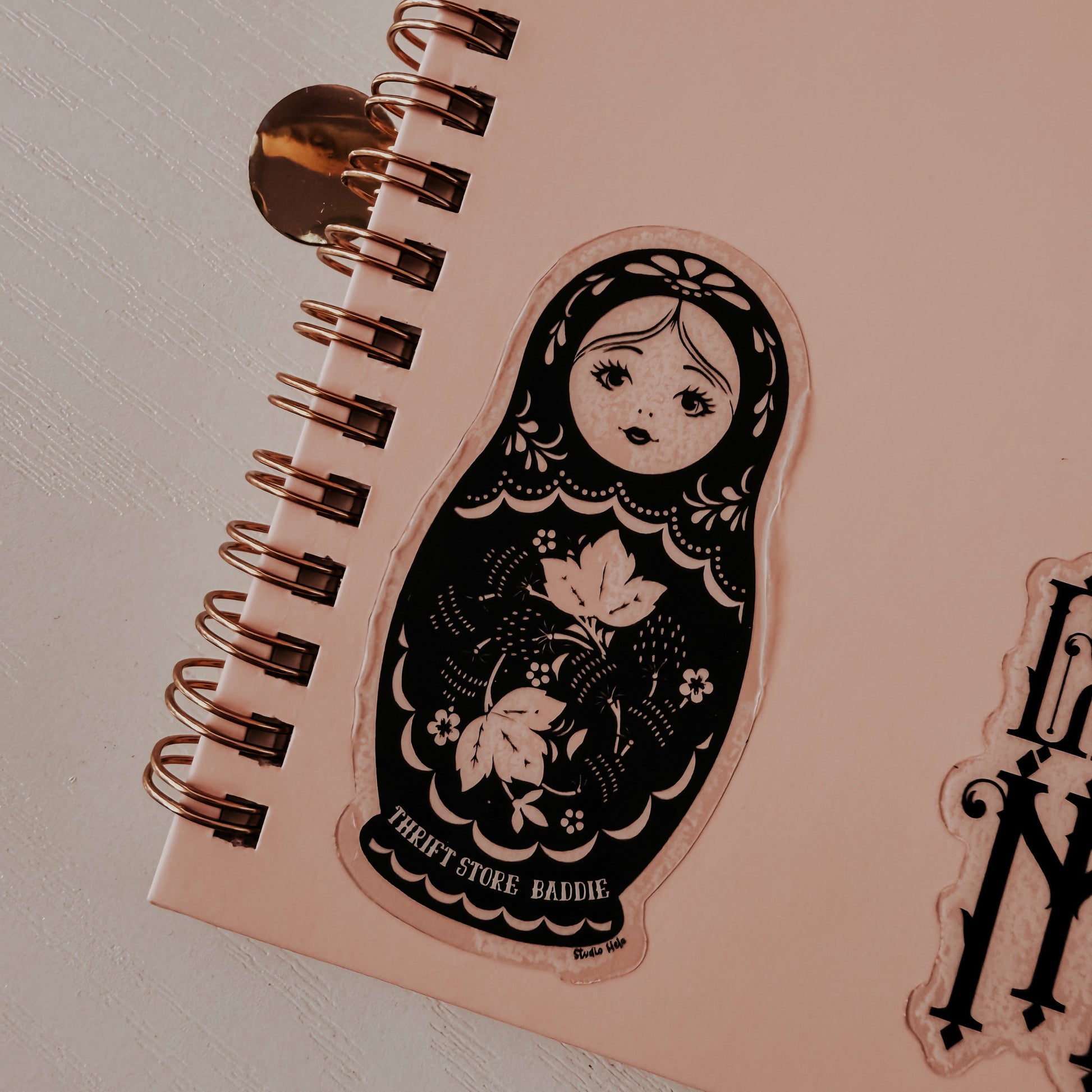 Pink notebook with a decorative sticker of a matryoshka doll on a light gray background
